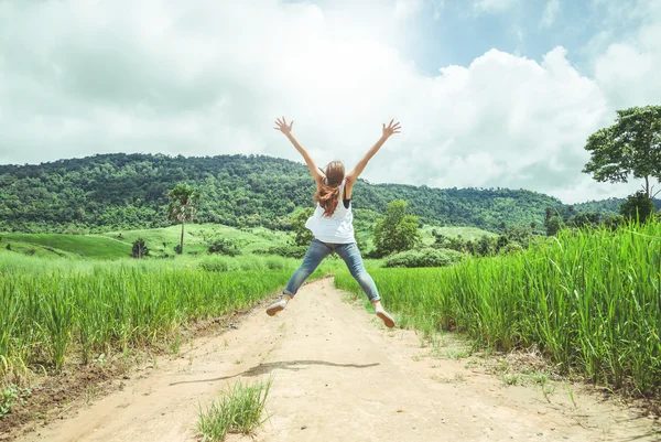 Een vrouw springt op een pad in een groene vallei